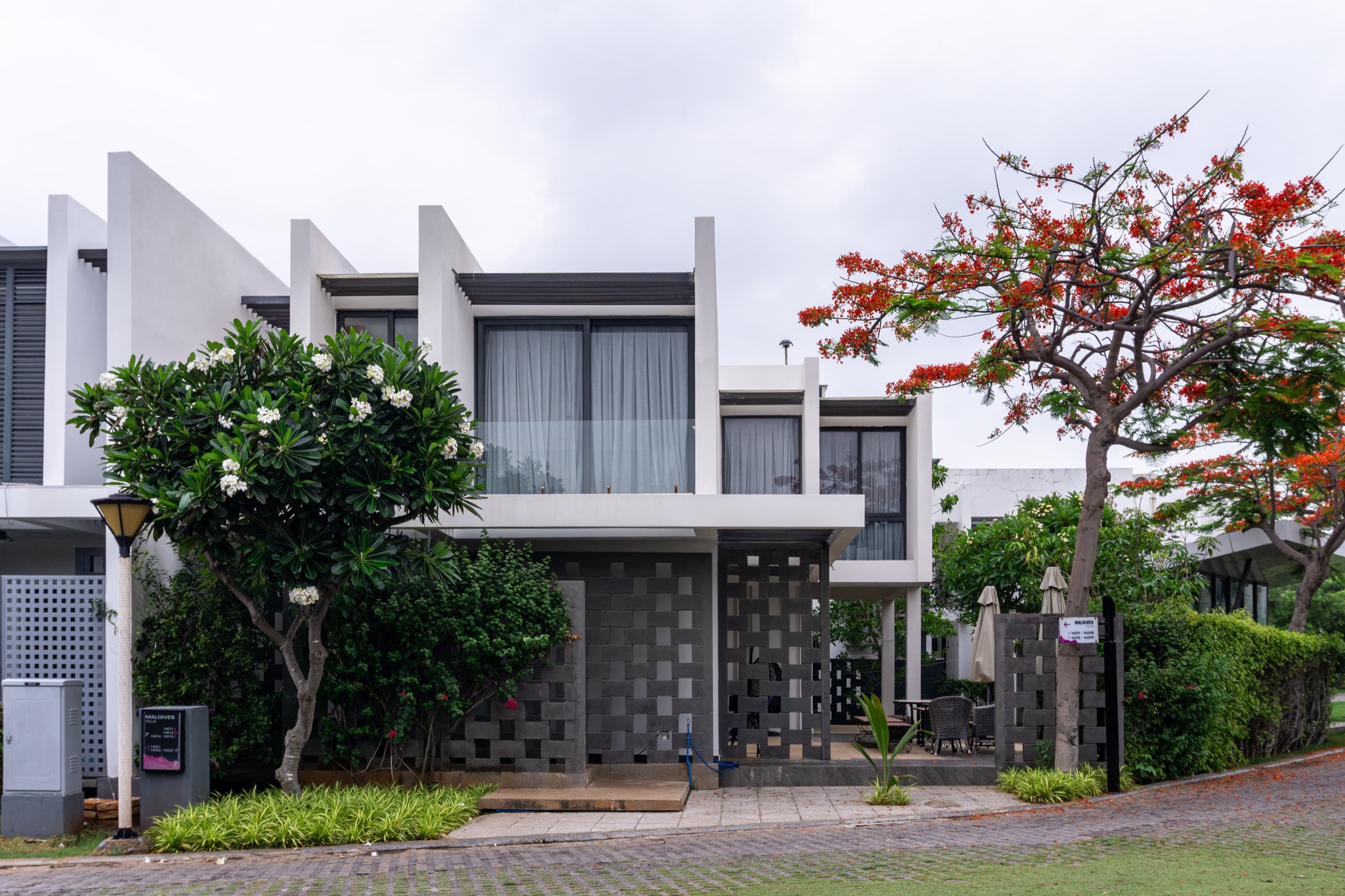 White modern facade of Oceanami Villa framed by frangipani and flame trees